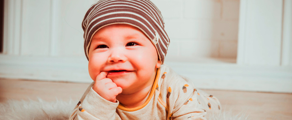 Smiling baby biting the right index finger