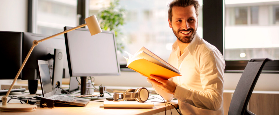 Man in an office holding a book.