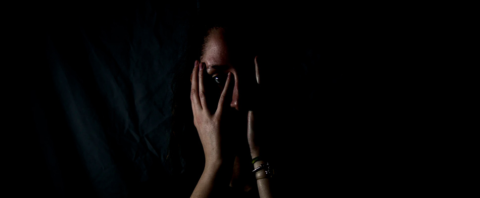 Woman holding her face in dark room.