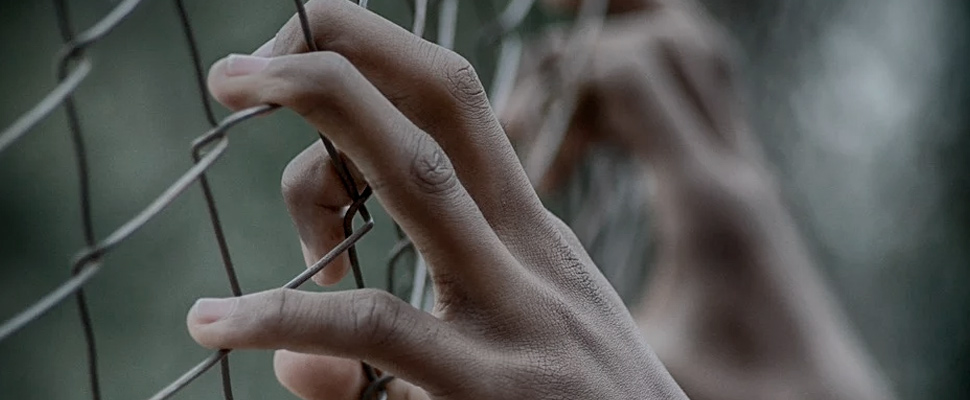 Man in prison with his hands on the fence.