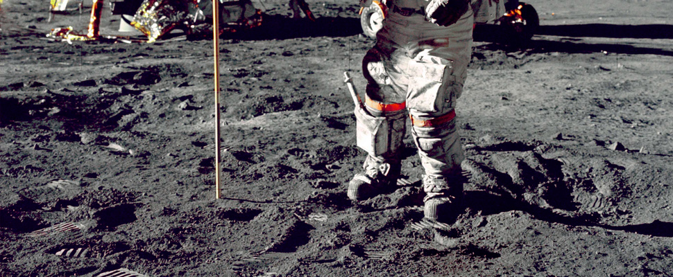 Astronaut standing on moon beside the USA flag.