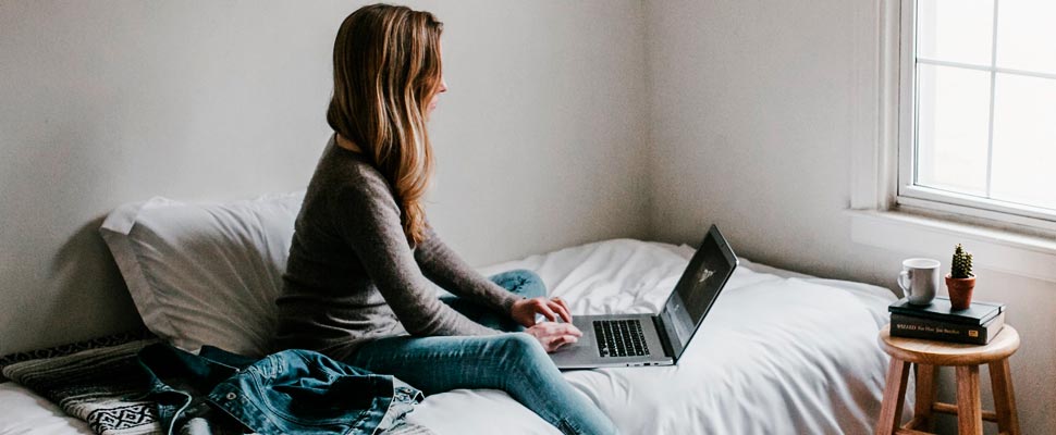 Woman sitting on the bed using her laptop.