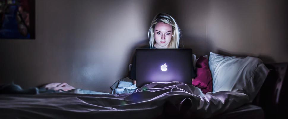 Woman working on her computer from her bed