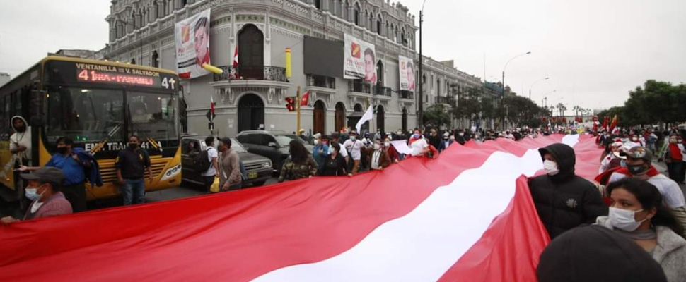 Peruvians marching in the streets holding a flag of Peru.