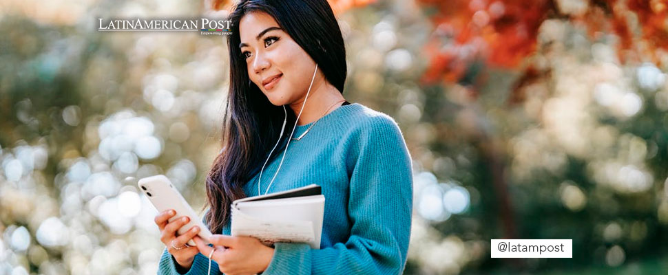 Mujer escuchando música con audífonos mientras sostiene un cuaderno